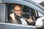 man with glasses sits in the driver's seat of a car, ready to drive