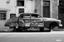 monochrome photograph of a classic car adorned with a sign